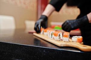 Feche as mãos do chef profissional vestindo luvas pretas fazendo sushi e pãezinhos em uma cozinha de restaurante de comida tradicional japonesa. foto