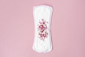 almofada menstrual com confete vermelho como gotas de sangue no fundo rosa pastel. conceito minimalista de higiene feminina durante a menstruação. vista do topo. foto