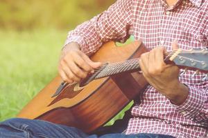 guitarra acústica de cara elegante hipster tocando à mão. artista homens músico tocando violão no parque público. foto