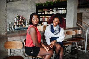 Atraente americano africano duas amigas sentadas em cadeiras contra bar no pub. foto