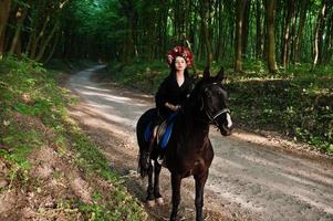 garota mística em grinalda veste de preto a cavalo em madeira. foto
