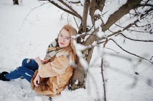 retrato de menina loira de óculos, casaco de pele vermelho e cachecol em dia de inverno. foto