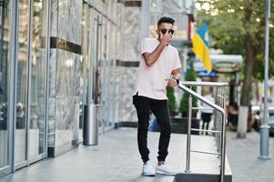 homem de barba indiana elegante em óculos de sol e camiseta rosa. modelo da índia posou ao ar livre nas ruas da cidade. foto