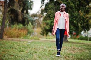 jovem mulher muçulmana africana moderna elegante, atraente, alta e magra no lenço de cabeça hijab ou turbante e casaco rosa posou no parque. foto