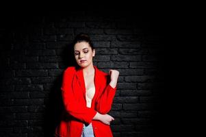 menina morena elegante na jaqueta vermelha contra a parede de tijolo preto do estúdio. foto