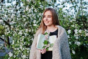 jovem morena na manta contra árvore de flor de primavera e segurando o livro nas mãos. foto