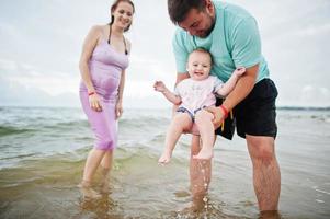 férias de verão. pais e pessoas atividade ao ar livre com crianças. boas férias em família. pai, mãe grávida, filha bebê na praia de areia do mar. foto