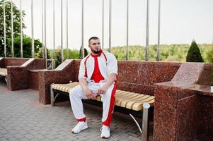 jovem homem musculoso barbudo brutal usar terno branco esporte com camisa vermelha. foto