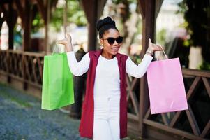 garota afro-americana casual com sacolas coloridas andando ao ar livre. mulher negra elegante às compras. foto