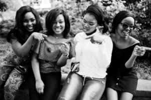 grupo de quatro garotas afro-americanas sentadas ao ar livre e mostrando os dedos. foto