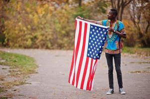 homem africano na camisa tradicional da África no parque outono com bandeira dos eua. foto