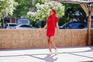 linda e magra garota afro-americana de vestido vermelho com dreadlocks em movimento se divertindo na rua. elegante modelo preto. foto