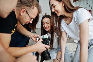 a equipe de fotógrafos mostrando fotos na tela da câmera para gêmeas modelos meninas no estúdio. fotógrafo profissional no trabalho.