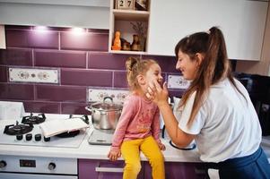 mãe com filha cozinhando na cozinha, momentos infantis felizes. mãe beijar seu bebê. foto