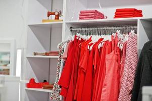 conjunto de roupas coloridas vermelhas femininas nas prateleiras e prateleiras na loja de roupas nova boutique moderna. coleções de vestidos de primavera verão. foto