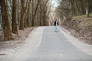 homem árabe de estilo de rua em óculos com longboard longboard na estrada. foto