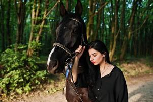 garota mística veste de preto com cavalo em madeira. foto