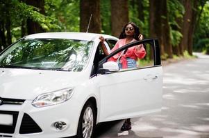 mulher afro-americana posou contra carro branco na estrada florestal. foto