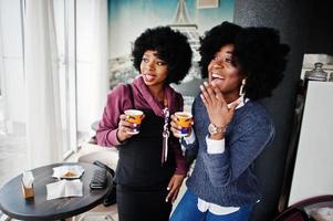 duas mulheres afro-americanas de cabelo encaracolado usam suéteres com xícaras de chá posadas no café interior. foto