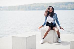 modelo magro de pele escura afro-americana posou em um short preto e jaqueta jeans contra o lado do mar. foto