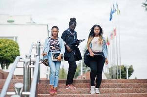 três estudantes africanos femininos posaram com mochilas e itens escolares no pátio da universidade. foto