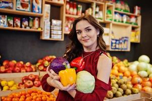 garota de vermelho segurando diferentes vegetais na loja de frutas. foto
