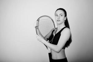 retrato preto e branco do jogador de mulher jovem e bonita em roupas esportivas, segurando a raquete de tênis em pé contra um fundo branco. foto