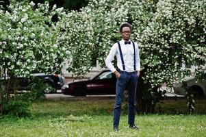 homem de negócios americano africano elegante em calças com suspensório e camisa com gravata borboleta, chapéu e óculos posou ao ar livre. foto