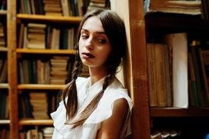 menina com tranças na blusa branca na antiga biblioteca. foto