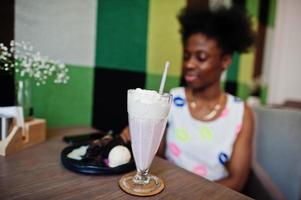 feche o coquetel de milk-shake contra alegre jovem afro-americana no vestido de verão no café. foto
