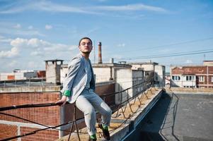 sonhador elegante macho de terno cinza, chapéu e óculos posou no telhado. foto