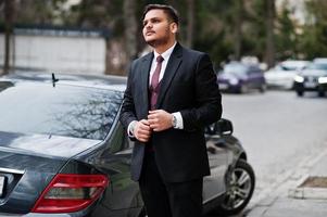 elegante empresário indiano com roupa formal em pé contra carro preto na rua da cidade. foto
