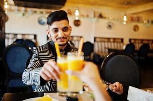 feche as mãos do lindo casal indiano apaixonado, sentado no restaurante e torcendo juntos por suco de laranja. foto