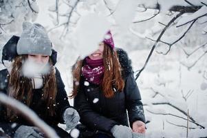 duas amigas engraçadas se divertindo no dia de inverno nevado perto de árvores cobertas de neve. foto