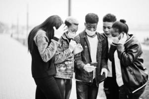 grupo de amigos adolescentes africanos no parque usando máscaras médicas protegem contra infecções e doenças quarentena de vírus coronavírus, leia notícias chocadas no telefone. foto