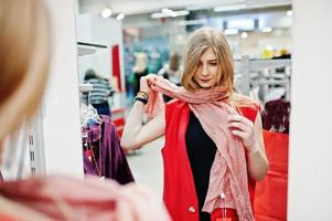 loira experimenta um vestido vermelho na boutique, olhando no espelho. foto