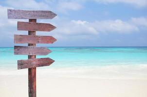 sinais de madeira para direções de viagem na praia com fundo de mar e céu azul. foto