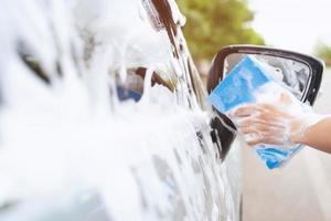 homem trabalhador de pessoas segurando a mão esponja azul e janela de limpador de espuma de bolha para lavar o carro. lavagem de carro de conceito limpa. deixe espaço para escrever mensagens. foto