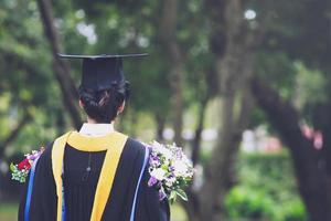 atirou no verso jovem estudante na mão segurando um buquê de flores os graduados de chapéus de formatura durante graduados de sucesso de início da universidade, parabéns educação de conceito. foto