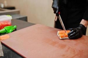 Feche as mãos do chef profissional vestindo luvas pretas fazendo sushi e pãezinhos em uma cozinha de restaurante de comida tradicional japonesa. foto