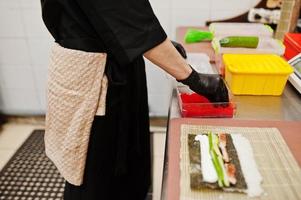 Feche as mãos do chef profissional vestindo luvas pretas fazendo sushi e pãezinhos em uma cozinha de restaurante de comida tradicional japonesa. foto