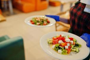 garçom em luvas segura pratos com salada no restaurante italiano. foto