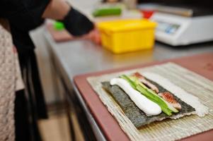 Feche as mãos do chef profissional vestindo luvas pretas fazendo sushi e pãezinhos em uma cozinha de restaurante de comida tradicional japonesa. foto