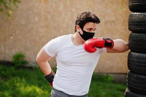 retrato esportivo homem boxer árabe em máscara facial médica preta boxe ao ar livre durante a quarentena de coronavírus. foto