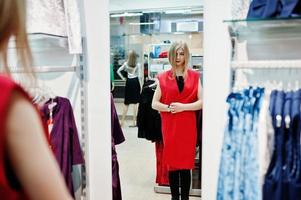 loira experimenta um vestido vermelho na boutique, olhando no espelho. foto