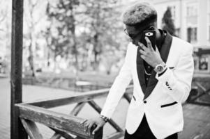 homem afro-americano bonito chique de terno branco com telefone celular na mão. foto