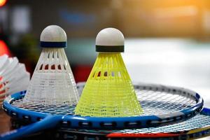 peteca de badminton de plástico branco e amarelo e raquete com sombreamento de luz neon no chão verde na quadra de badminton indoor, fundo de badminton desfocado, espaço de cópia. foto