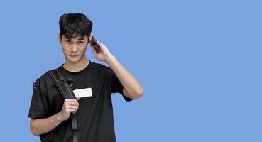 isolado jovem adolescente masculino asiático em camiseta preta, olhando para a câmera e segurando o celular e a bolsa preta atrás, foco suave e seletivo. foto