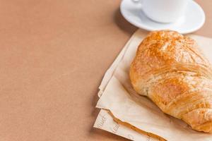 saboroso café da manhã. croissant francês servido na chapa branca e xícara de café preto ou expresso em fundo marrom. copie o espaço. foto