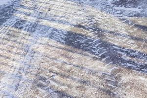 trilhas de rodas na estrada de inverno coberta de neve em um dia ensolarado foto